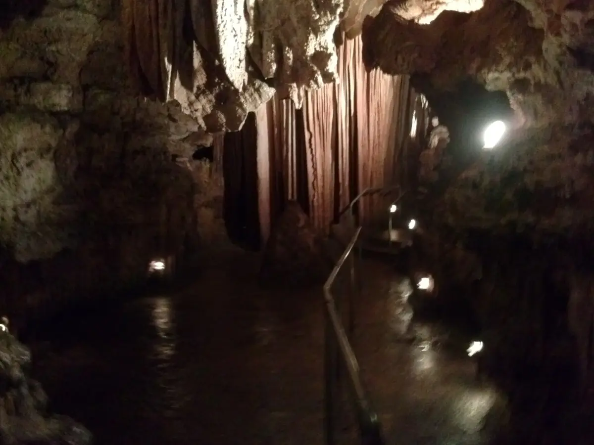 Lit passage with dark water and hanging rock curtains inside Bridal Cave