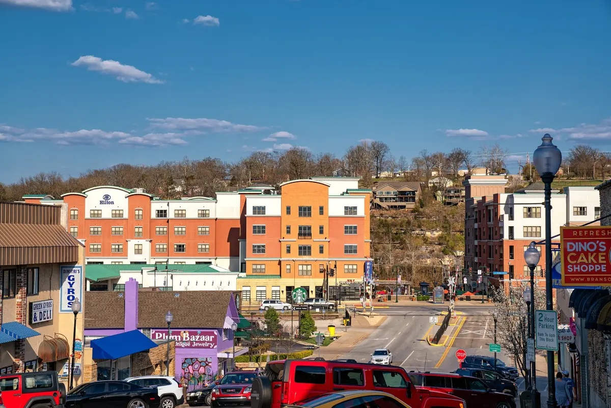 Downtown Branson street with colorful buildings climbing a hillside under blue sky