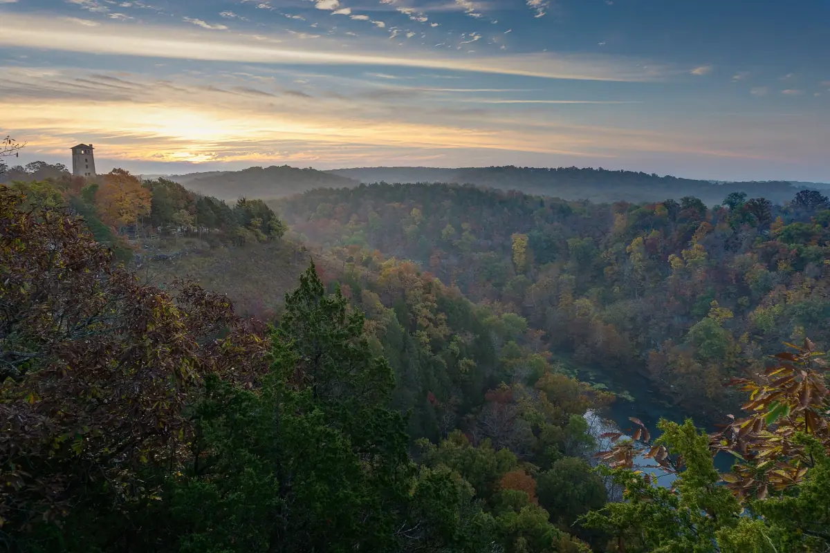 Hazy sunrise light over wooded hills and a river valley with a stone tower at Ha Ha Tonka