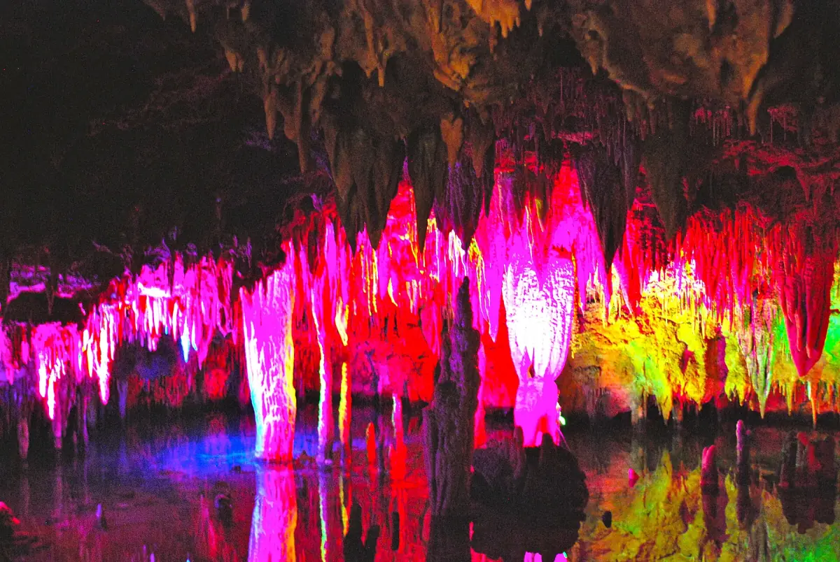 Rosa und gelb angestrahlte Stalaktiten spiegeln sich im stillen Wasser der Meramec Caverns
