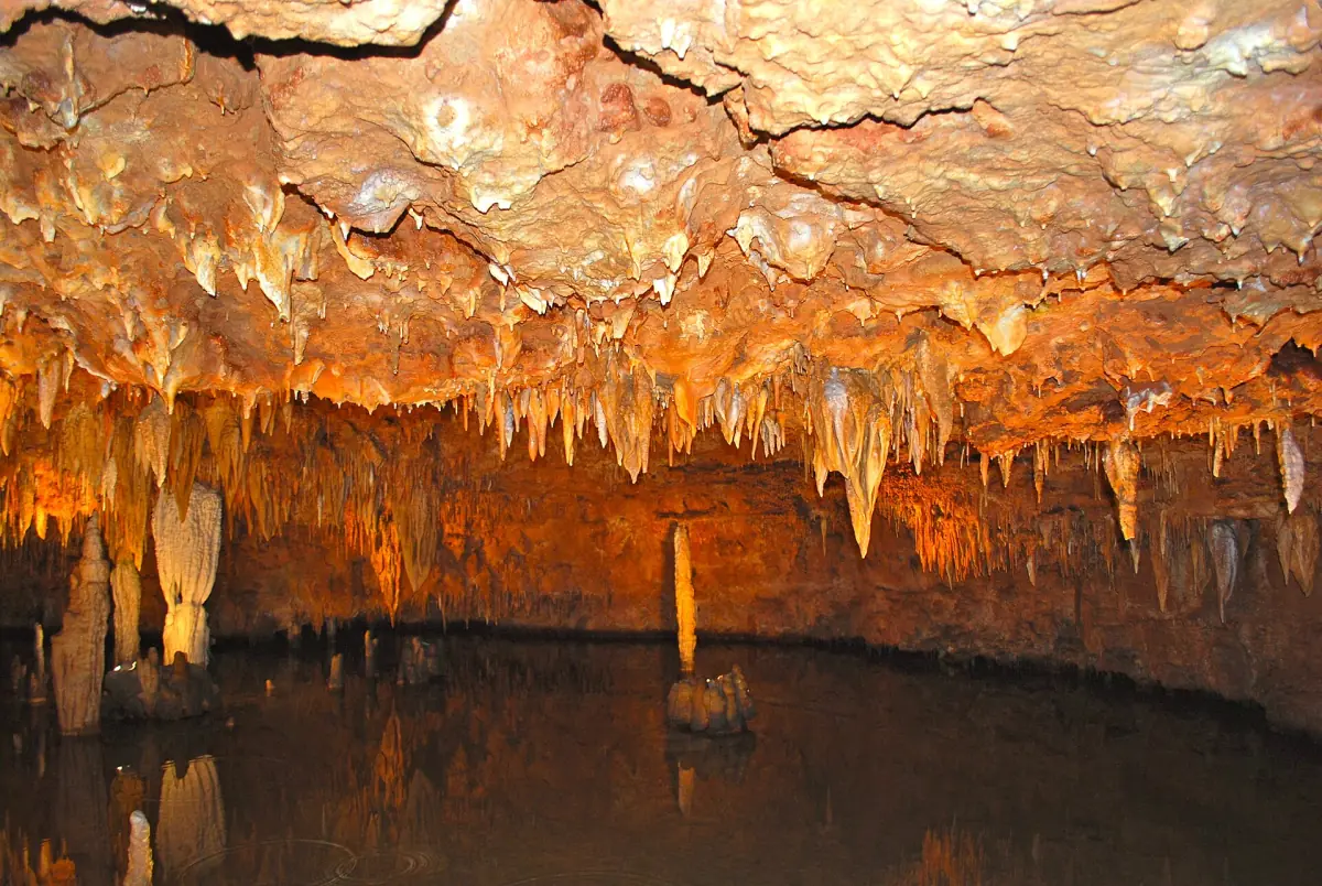 Orangefarbene Höhlendecke mit kleinen Stalaktiten über einem ruhigen Wasserbecken in den Meramec Caverns