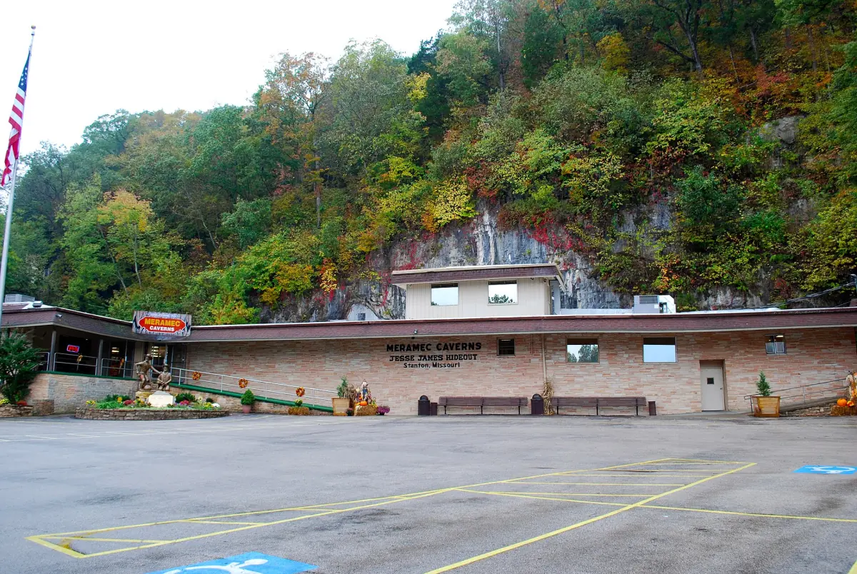 Visitor center of Meramec Caverns at the foot of a wooded bluff with a parking lot